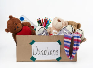 brown cardboard box filled with soft toys, school supplies on white background, concept of charity and help to needy children